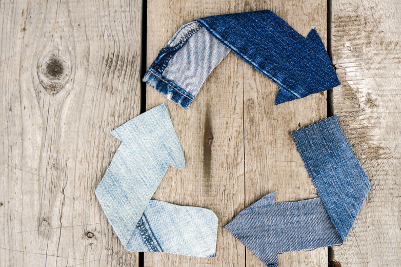 Wood background with denim pieces arranged as recycling symbol